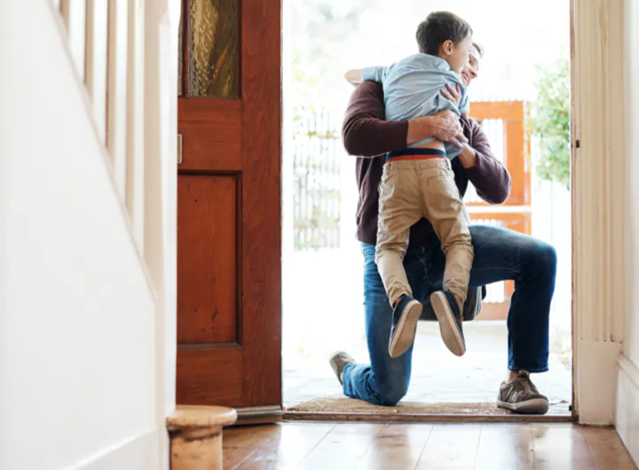 A young boy runs into his father’s arms at the front door.