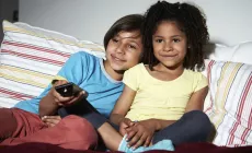 girls sitting on couch, sharing TV remote control 