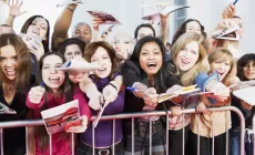 crowd of fans behind a fence screaming and waving autograph books