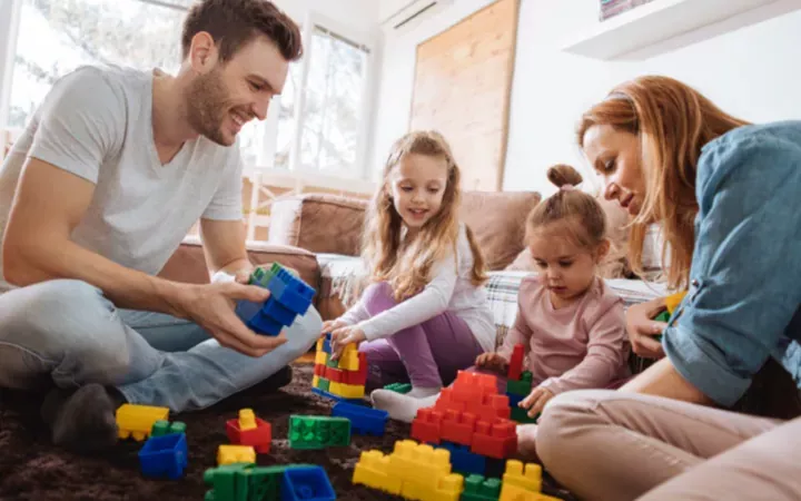 Une famille de quatre personnes assises par terre, jouant ensemble avec des blocs de construction colorés.