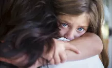 upset little girl looks over mom's shoulder as she gets a hug