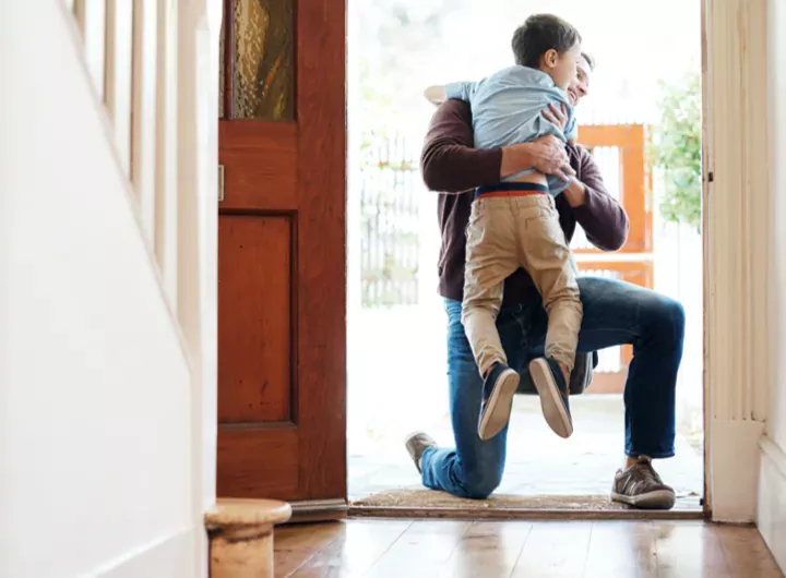 A young boy runs into his father’s arms at the front door.