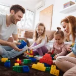 Une famille de quatre personnes assises par terre, jouant ensemble avec des blocs de construction colorés.